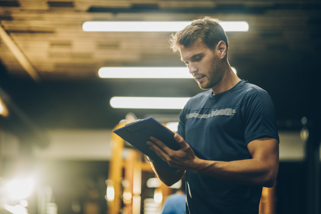 Young fitness instructor reading a training plan in a gym.